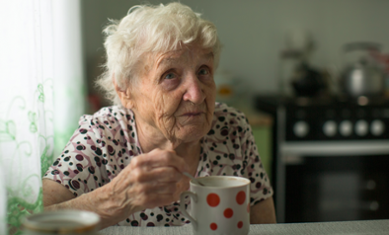 Äldre kvinna dricker te i sitt kök