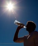 Man dricker ur vattenflaska med solen i bakgrunden