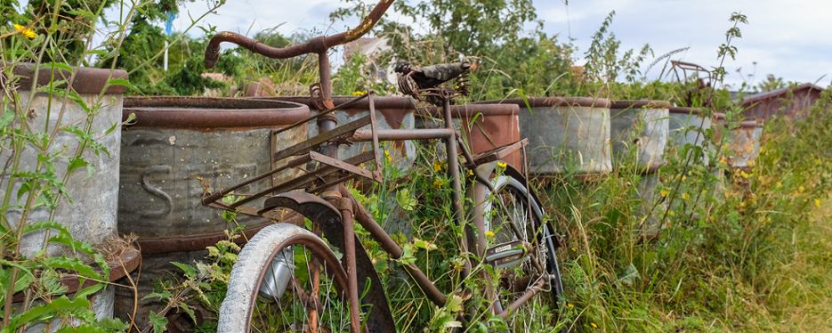 En gammal rostig cykel står lutad mot rostiga gamla tunnor.