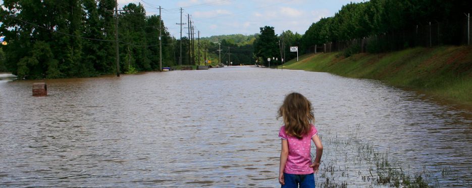 Liten flicka blickar ut över en översvämmad bilväg.