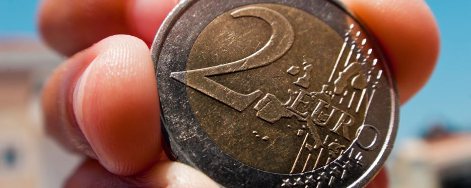 Närbild på ett 2 euro-mynt som någon håller i.
