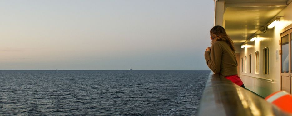 Kvinna lutar sig lätt mot relingen på en passagerarbåt och tittar framåt. En båt i horisonten.