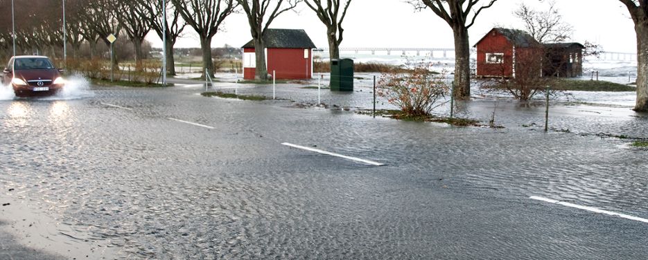 Bil kör på översvämmad väg nära havet.